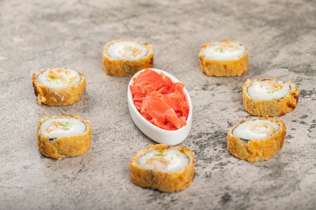 Fresh delicious sushi rolls with pickled ginger slices placed on a stone table .