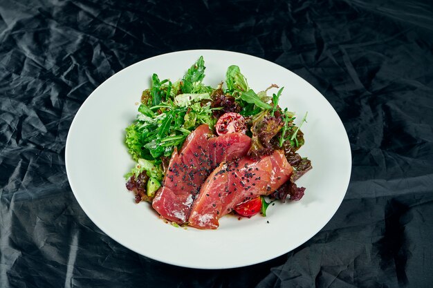 Fresh and delicious Tataki salad with tuna, lettuce, avocado. Tasty seafood salad of Japanese cuisine in white bowl on wooden table. Close up food photo