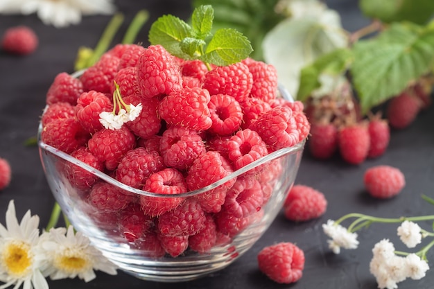 Fresh Deluxe Raspberries in glass bowl with field flowers on dark wooden