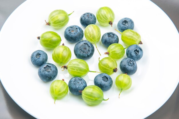 Фото Свежие разные ягоды на белой тарелке. полезный витамин здорового питания фрукты. здоровый овощной завтрак