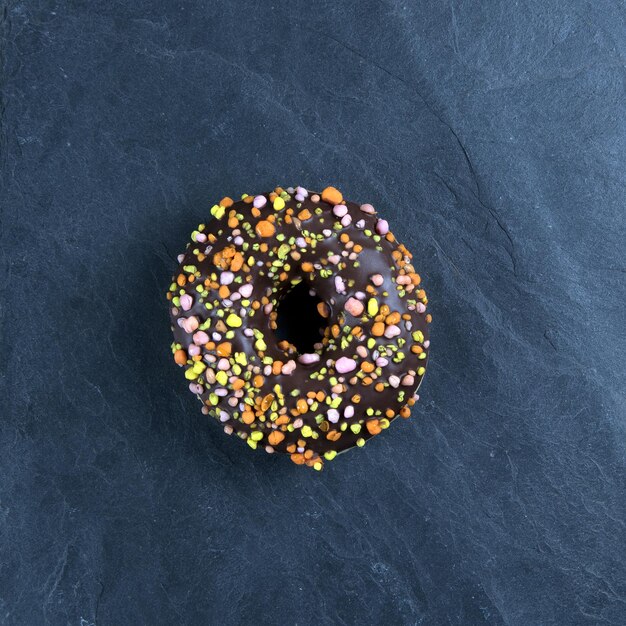 Fresh donut with toppings on a dark background.