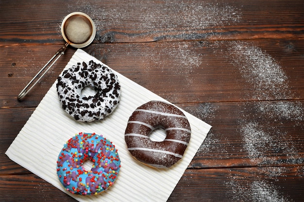 Fresh donuts sprinkled with powdered sugar on wooden background flat lay