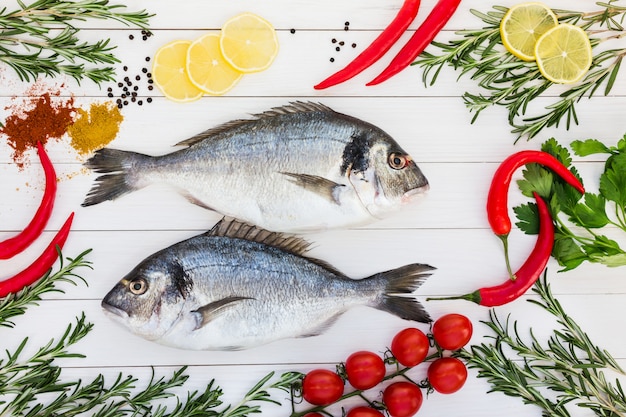 Fresh dorado fish, rosemary, lemon, cherry tomatoes, chilly pepper on white wooden table.