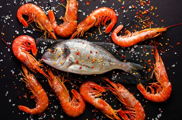 Fresh dorado fish and tiger prawns on black background