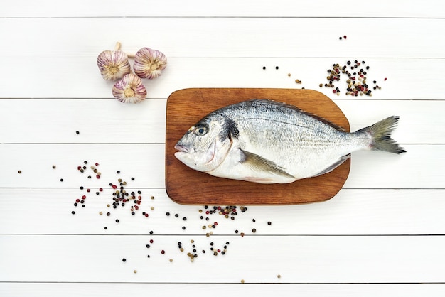 Fresh dorado fish on wooden cutting board with garlic and peppercorns. 