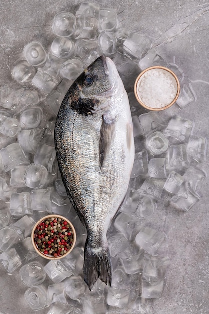 灰色の大理石の背景に氷の中で新鮮なドラドスパイスローズマリーペッパーと生の魚健康的な農場のシンプルな食べ物