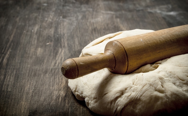 Fresh dough with a rolling pin. On a wooden table.