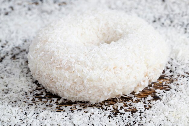 A fresh doughnut covered with white chocolate and sprinkled with coconut chips, a delicious and sweet doughnut dessert with a creamy filling, a high-calorie snack for lunch