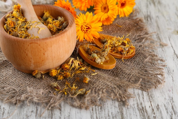 Fresh and dried calendula flowers in mortar on wooden background