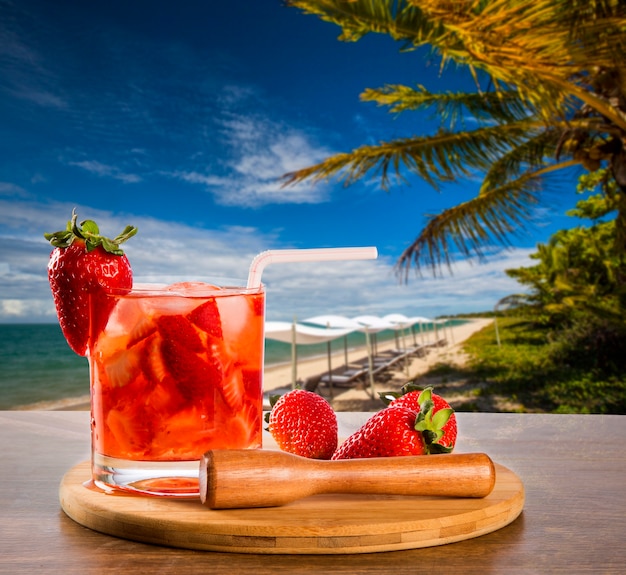 해변 배경에서 신선한 음료를 만든 딸기 Caipirinha