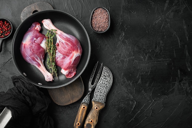 Cosce di carne di coscia di anatra fresca impostato sulla padella in ghisa per friggere sul piano del tavolo in pietra nera vista piatta laici