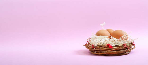 Fresh eggs in a beautiful nest on a pink background with copy space Banner Easter concept