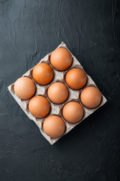 Fresh eggs on paper egg box set, on black background, top view flat lay