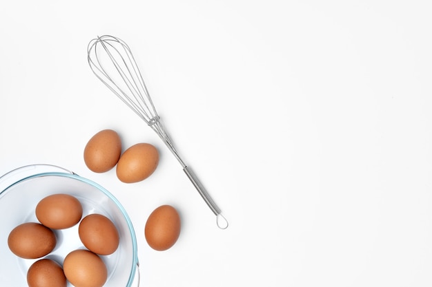 Fresh eggs with whisk isolated on white background