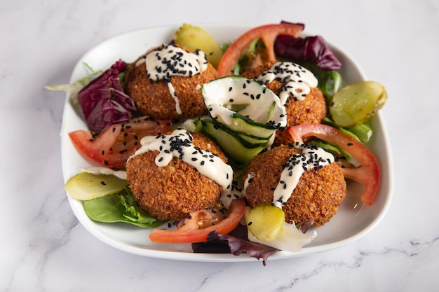 Fresh falafel with vegetables and tzatziki sauce on white plate on marble table