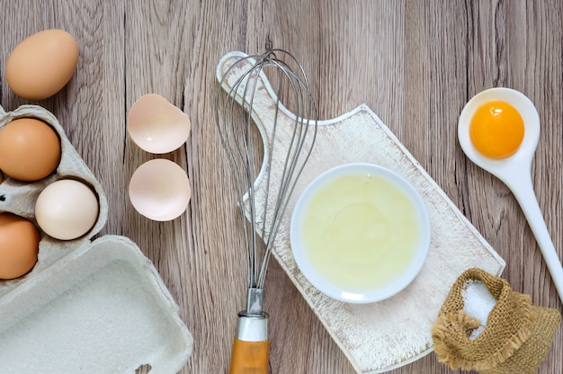 Fresh farm eggs on a wooden rustic background. Separated egg white and yolks, broken egg shells. Whipping eggs with whisk.