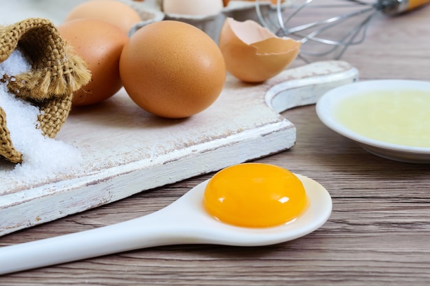 Свежие яйца фермы на деревянном деревенском фоне. Отделенный яичный белок и желтки, разбитые скорлупы яиц. Взбивать яйца венчиком.