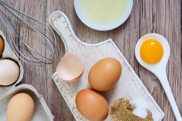 Fresh farm eggs on a wooden rustic background. Separated egg white and yolks, broken egg shells. Whipping eggs with whisk.