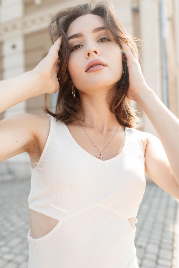 Photo 街でポーズをとるトレンディな白いドレスでかわいいきれいな肌の顔を持つ美しいスタイリッシュな女の子の新鮮な女性の肖像画