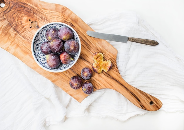 Fresh figs in blue patterned ceramic bowl and on olive wood board over white background