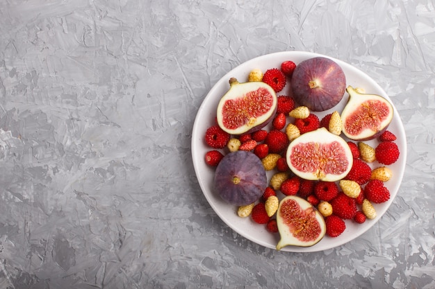 Fresh figs, strawberries and raspberries on gray concrete. top view