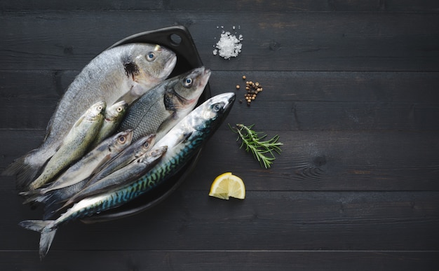 Photo fresh fish in black bowl on wooden background. top view.