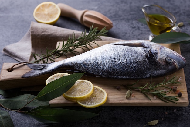 Fresh fish dorado on cutting board on grey stone table with ingredients for cooking. Top view with copy space.