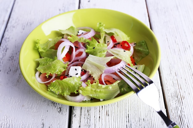 Fresh fish salad with vegetables on plate on wooden table closeup