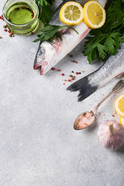 Fresh fish Sea Bass raw with salt pepper parsley olive oil and lemon on cutting board on light gray concrete rustic background Food cooking background Top view copy space
