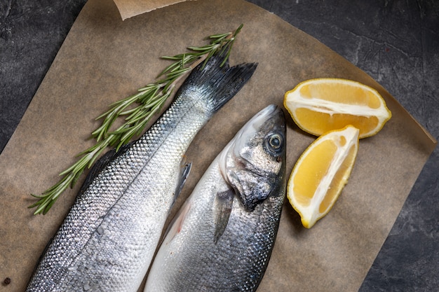 Spigola di pesce fresco e ingredienti per cucinare, limone e rosmarino