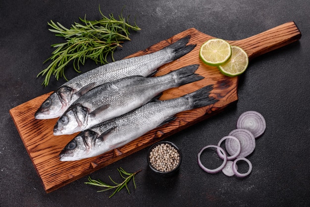 Fresh fish seabass and ingredients for cooking. Raw fish seabass with spices and herbs on a dark table