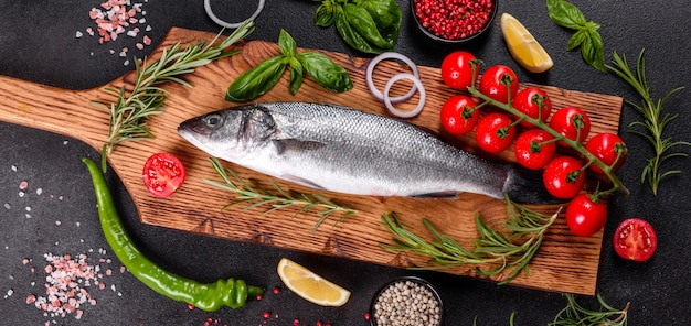 Spigola di pesce fresco e ingredienti per cucinare. branzino di pesce crudo con spezie ed erbe aromatiche su un tavolo scuro