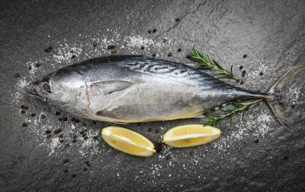 Fresh fish with herbs spices rosemary and lemon Raw fish seafood on black plate background top view Longtail tuna Eastern little tuna fish