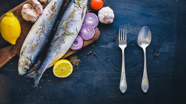 Pesce fresco con verdure, spezie e olio su fondo di legno nero spazio libero per il testo vista dall'alto