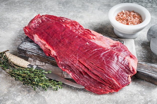 Foto bistecca di manzo cruda fresca di fianco o lembo su tavola di legno con erbe aromatiche. sfondo grigio. vista dall'alto.