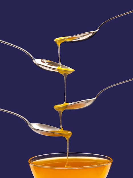 Photo fresh floral honey drips from a spoon into a spoon on a blue background. organic vitamin food.