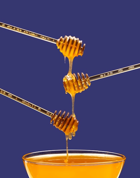 Fresh floral honey drips from a spoon into a spoon on a blue background. Organic vitamin food.