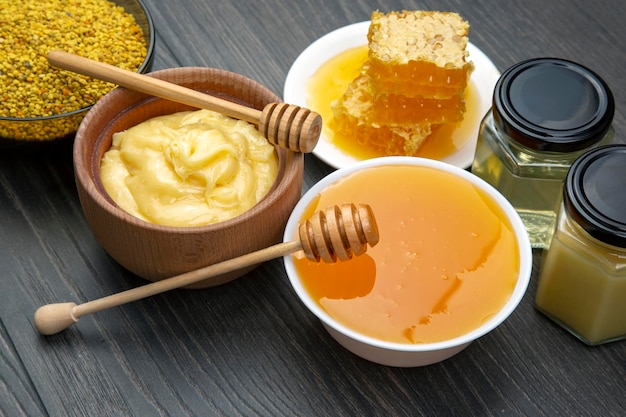 Свежий цветочный мед разных сортов, пыльца и соты с ложками на деревянном фоне. Органическая витаминная здоровая пища