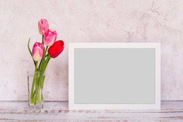 Fresh flowers in vase near frame