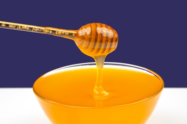 숟가락에서 파란색 배경에 접시로 떨어지는 신선한 향기로운 꿀. 유기농 비타민 영양
