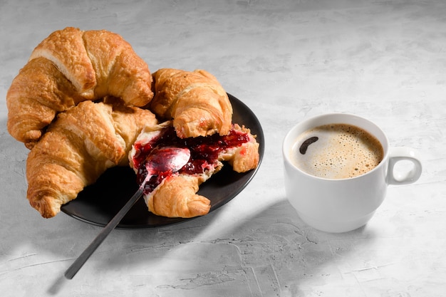 Fresh french croissant with cherry jam on grey plate and cau of fresh coffee