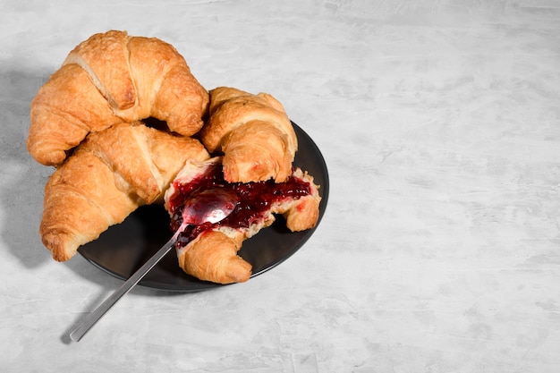 Fresh french croissant with cherry jam on grey plate on gray background