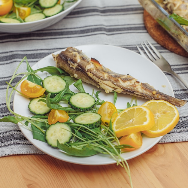 Il pesce fritto fresco con le verdure è servito sul piatto sulla tavola di legno, primo piano