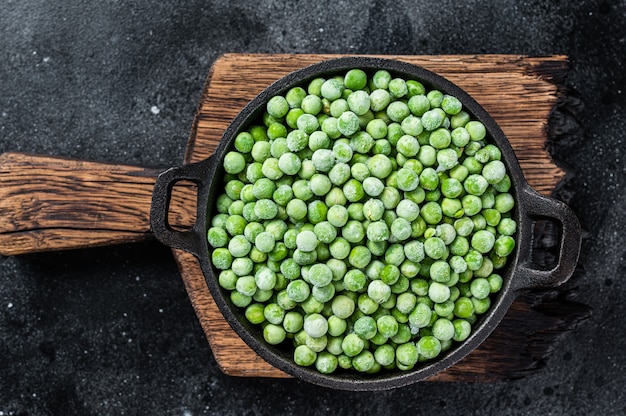 Fresh Frozen green peas in a pan. Black background. Top view.