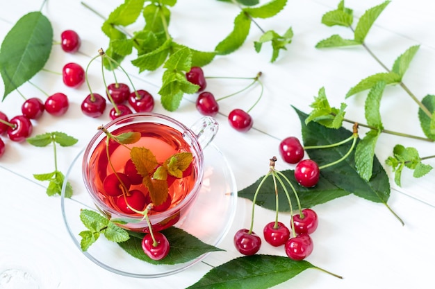 Fresh fruit cherry drink in transparent glass cup surrounded by cherries on the white wooden background Top view