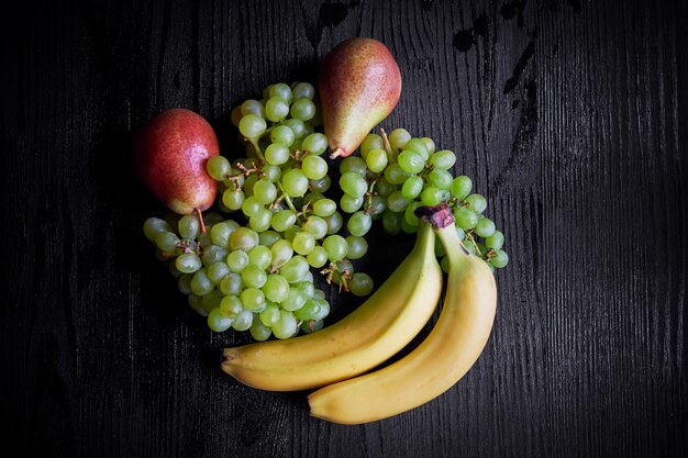 Fresh fruit on a dark background grapes pear and bananasHealthy eating