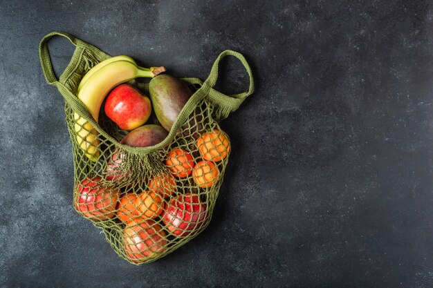 Fresh fruit in a green string bag. Bananas, apples, oranges, and mangoes.