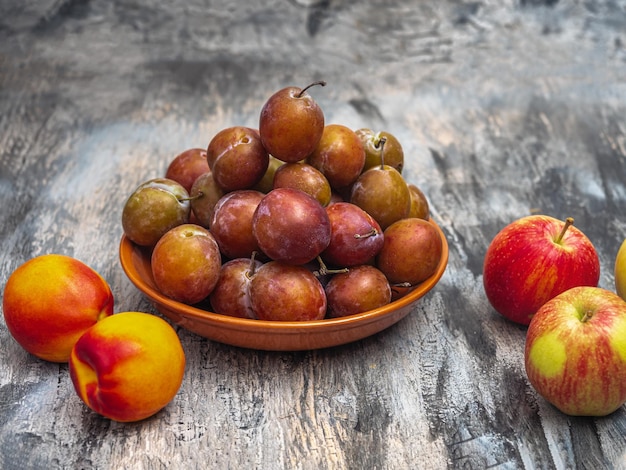 Frutta fresca per un pranzo leggero prugne su un piatto di argilla nettarine e mele