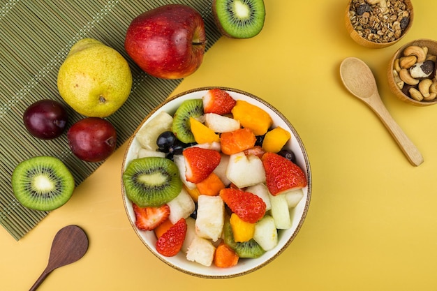 Photo fresh fruit salad in a bowl multicolored and tropical fruits pineapple mango grape strawberry papaya melon kiwi additional with chestnuts and granola top view selective focus