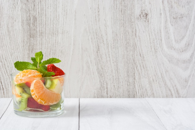 Fresh fruit salad in glass on wooden table copy space